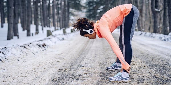 Femme habillée en vêtements de sport qui fait un étirement sur un sentier enneigé