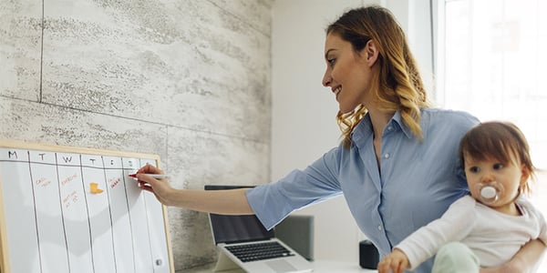 Femme avec enfant dans les bras qui prend des notes sur un tableau blanc