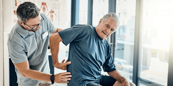 Homme assis sur une table qui pointe son dos et thérapeute debout