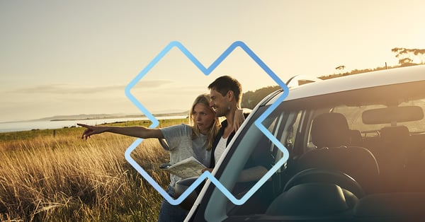 couple en road trip, consultant une carte papier près de leur voiture stationnée, avec vue sur la mer au coucher du soleil