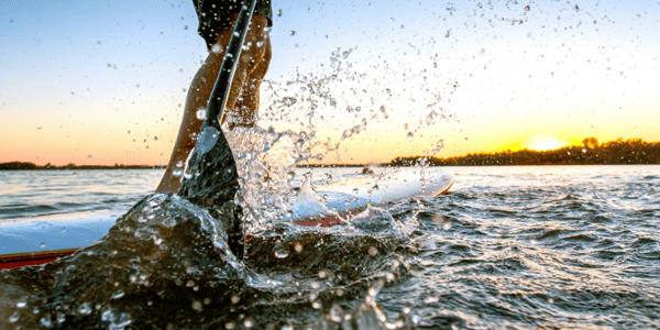 Personne qui rame debout sur une planche sur l'eau au coucher du soleil